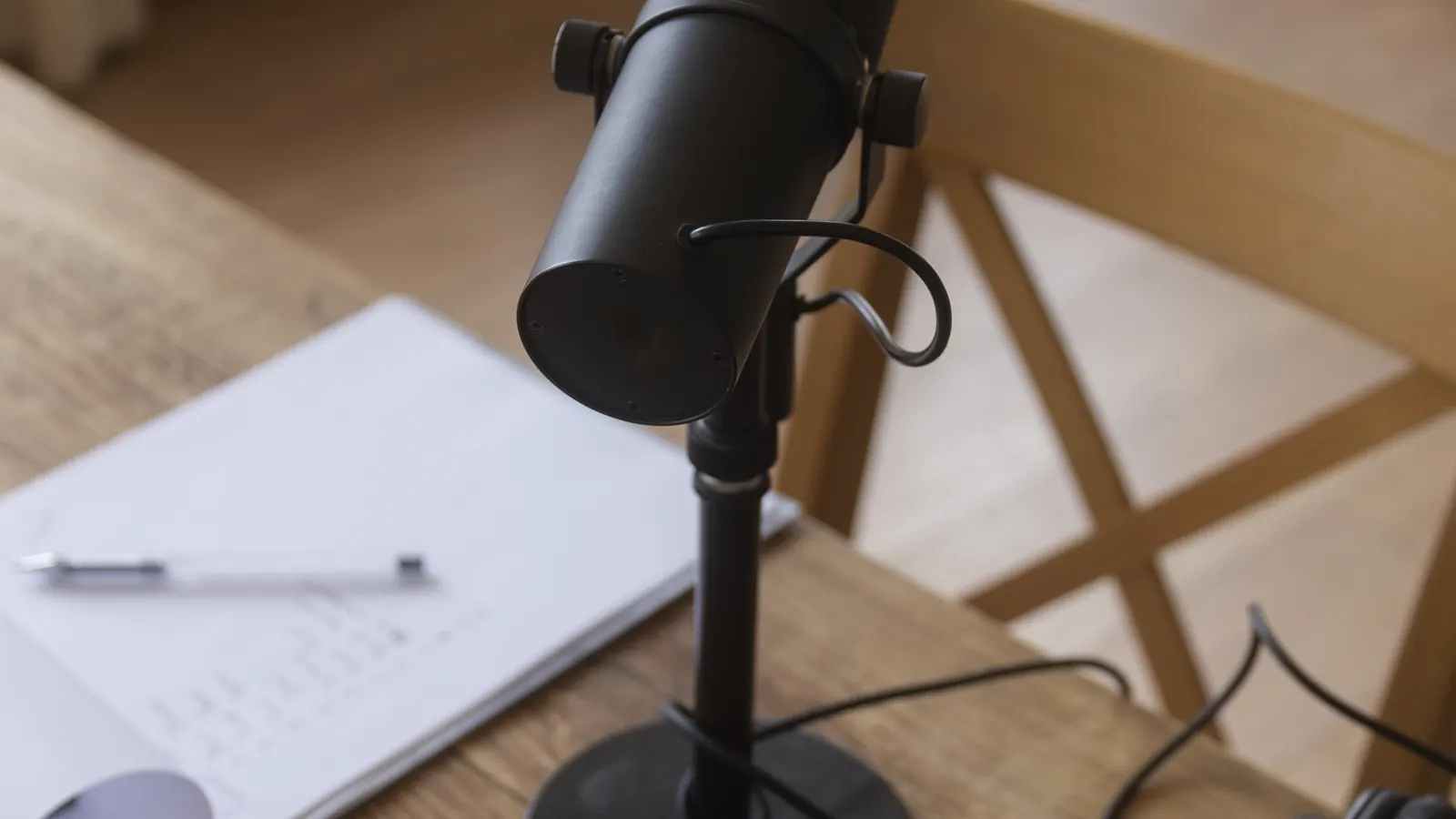 A black desk microphone on a stand next to a notepad on a wooden table.